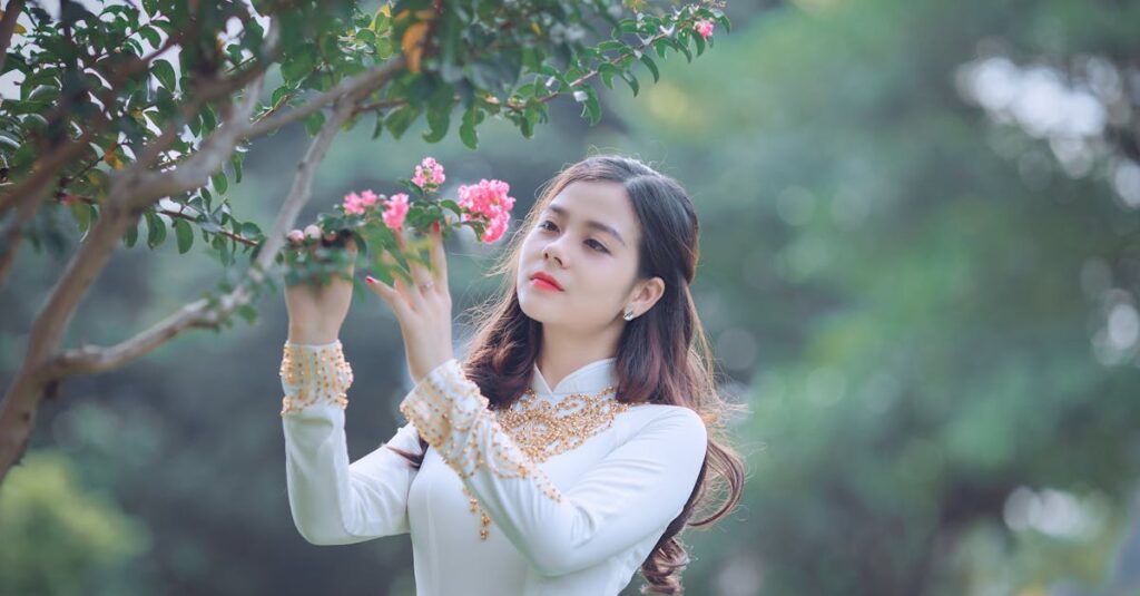 An elegant woman in traditional Ao Dai appreciating the beauty of pink blossoms.
